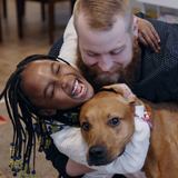 A dad holds his happy daughter as she hugs her dog